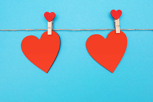 istock Two red decorative hearts are attached with clothespins to a rope on a blue background 2245215619