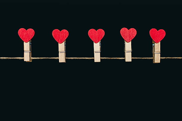 Clothespins decorated with red hearts hang on a rope on a black background. Concept for lovers. Valentine's Day holiday. Decor in the form of clothespins and free space for the designer