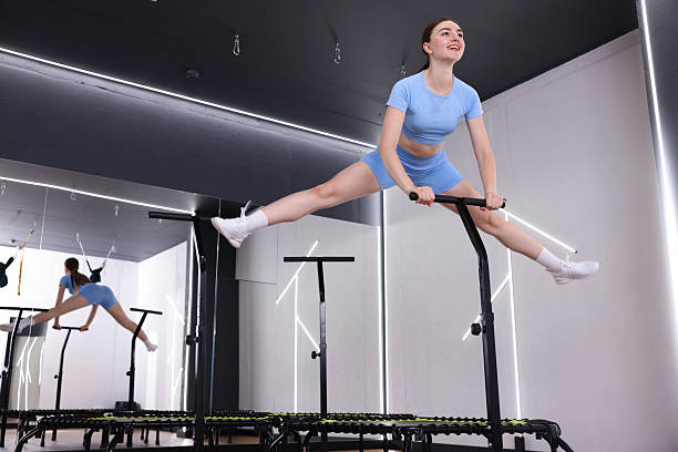 Smiling woman jumping on mini exercise trampoline in fitness studio, low angle view. Space for text