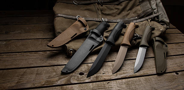istock Tactical fixed-blade knives and sheaths on a rustic wooden table and canvas bag. 2245218187