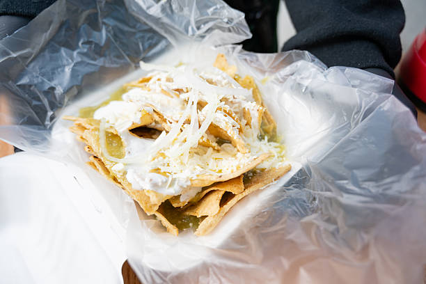 Chilaquiles with green salsa, cream, cheese, and onion served in a recyclable container, ready to enjoy as a traditional Mexican breakfast.