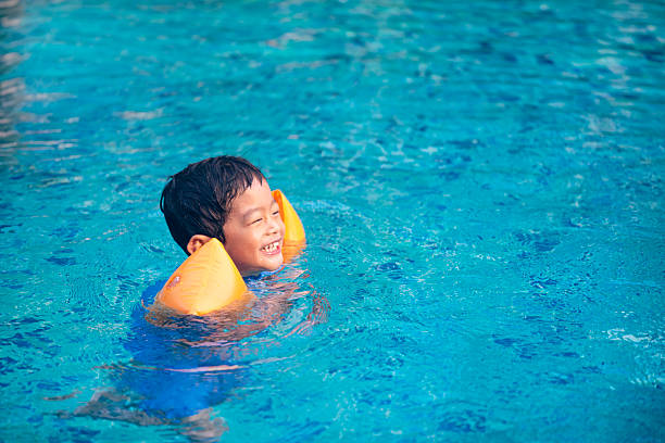 istock Asian Kid Swimming with Orange Arm Floats in Clear Blue Pool, Summer Learning and Fun 2245228068