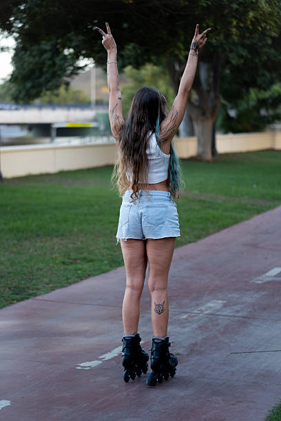 Woman with long hair and tattoos rollerblading outdoors, raising arms with peace signs, expressing joy and freedom