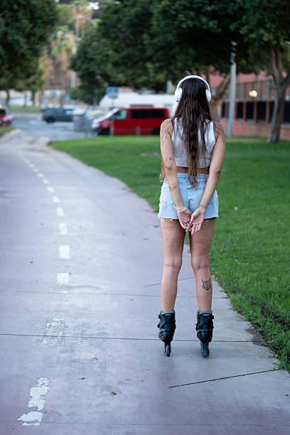 Young woman rollerblading outdoors, wearing headphones, enjoying music and leisure activity along a park path