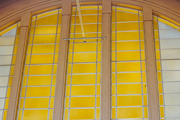 Close-up of a stained glass window featuring panels in yellow, blue, and green hues. Sunlight filters through the textured glass, casting a vibrant glow onto the interior. The image conveys creativity, color harmony, and the artistic beauty of architectural details.