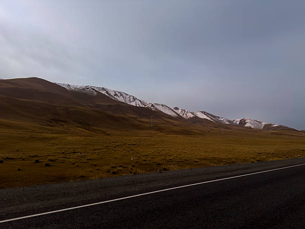 Soft sunlight breaks through the clouds, casting a warm glow across a quiet road and distant peaks.