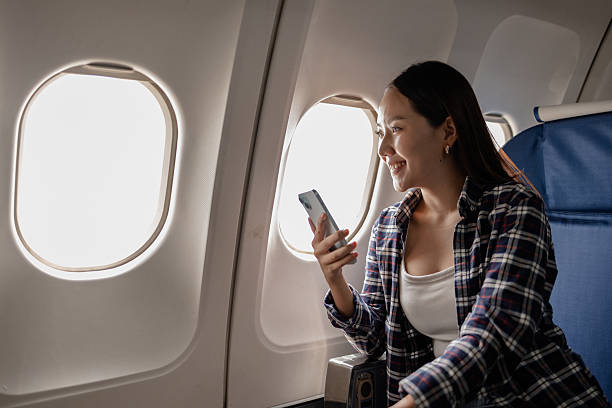 istock Asian woman smiling while using her smartphone on an airplane. She is sitting next to the window, enjoying her time during the flight. The atmosphere appears relaxed and comfortable. 2245243909