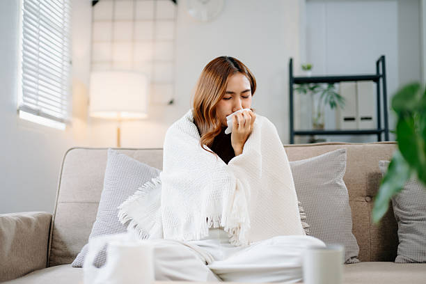 istock Young Asian woman suffering from flu symptoms, covered with a blanket on a sofa. Concept of illness, healthcare, and recovery. Stay indoors, stay healthy 2245245498