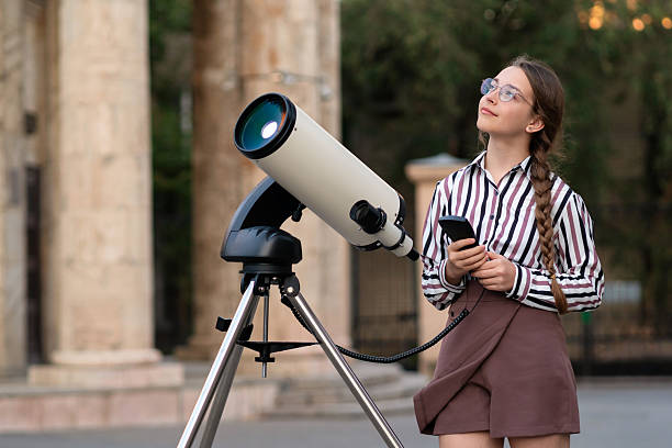 istock Girl gazing at sky while standing near mounted telescope 2245253533