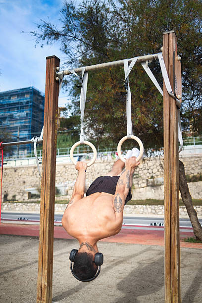 strong Latino man executing a front lever on wooden calisthenics rings at an outdoor fitness park. Concept of strength, balance, and body control in advanced calisthenics training.