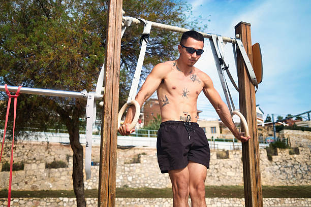 Fit Latino athlete performing arm push-ups using wooden calisthenics rings at outdoor gym