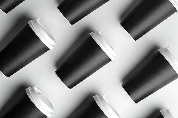 Multiple black takeaway coffee cups arranged in a repeating pattern on a white surface