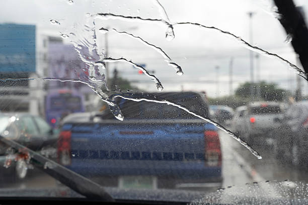 istock Rainy day traffic view through car windshield with raindrops and wipers showing blurred road background 2245259533