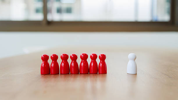 istock Leadership recruitment concept with single white figure separated from group of red figures on wooden table symbolizing teamwork and inclusion 2245264307