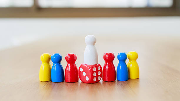 istock Leadership recruitment concept with white figure standing on red dice surrounded by yellow blue and red game pieces on wooden table 2245264336