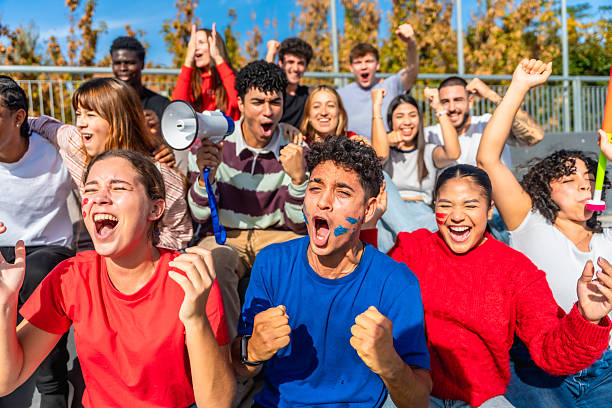 Exuberant diverse young adults watching a sports game, cheering loudly, with excited facial expressions, face paint, and team spirit, showing support for their favorite team