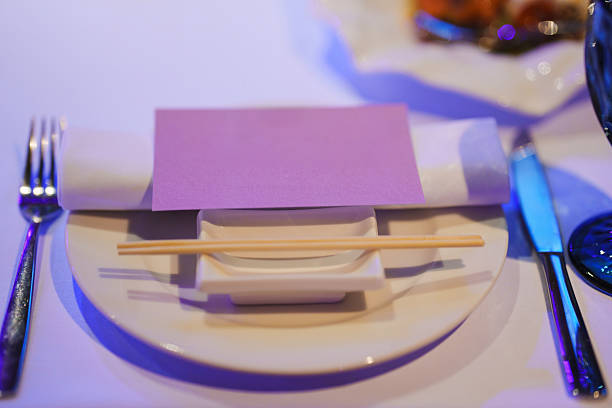 A beautifully arranged table features a white plate with chopsticks and a folded napkin resting on top. Soft lighting adds an inviting atmosphere, perfect for a dining event.