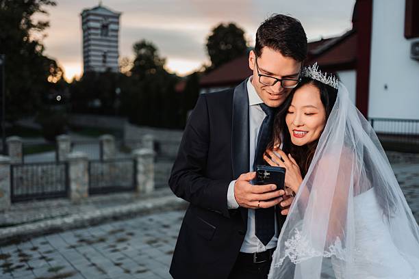 istock Happy bride and groom viewing content together on a mobile phone 2245269129