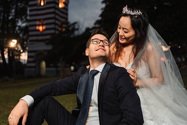 Happy bride and groom sitting on grass, looking at each other