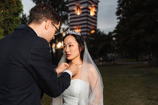 Groom adjusting bride's necklace during an outdoor ceremonial celebration at twilight