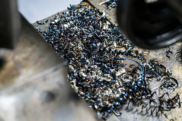 Close-up view of twisted metallic shavings resulting from a precision lathe machining process. The shavings are scattered across an industrial surface, showcasing various colors and textures created during machining.