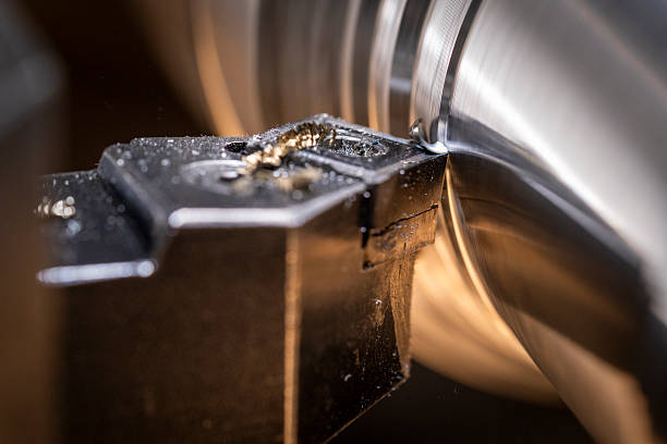 Close-up view of a lathe machine precisely cutting a metal piece. Metal shavings are visible as the tool carves into the material, highlighting the intricate work involved in metal turning within an industrial workshop environment.