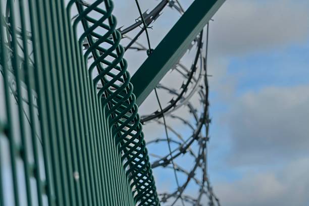 istock Barbed razor wire on a high-security building. Barbed wire and hard wire fence. Concepts for jails, army facilities, nuclear power plants, and defense against illegal migration. 2245271639