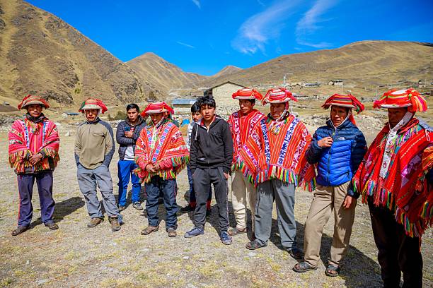 Cusco, Peru – July 04, 2020: A group of Quechua indigenous men in traditional attire stand in a mountainous landscape under a clear blue sky in Peru.