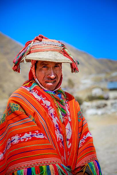 Cusco, Peru – July 04, 2020: Portrait of an quechua indigenous man wearing traditional colorful attire in a mountainous landscape under a clear blue sky.