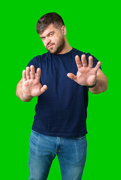 istock A man with a serious expression holds up both hands in a stopping gesture against a bright green background 2245272579