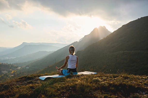 istock Woman meditating on mountain at sunrise with sunlight rays 2245272731