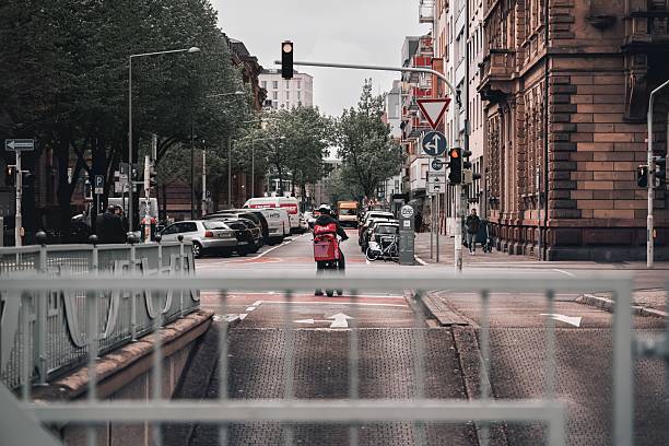 Mannheim, Germany – February 15, 2023: A delivery rider on a motorcycle waits at a red light in a busy European city street.