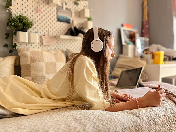 istock Thoughtful teen girl lying on bed while writing in notebook and watching screen 2245274207