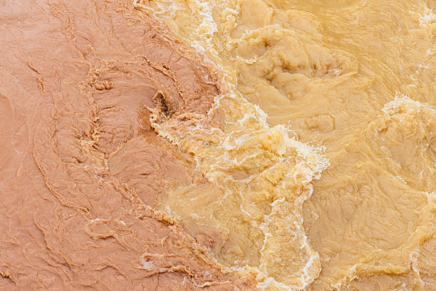 Muddy floodwaters with two different colors collide, showcasing water contamination, turbulence, and runoff caused by extreme rainfall and environmental disruption in disaster zones