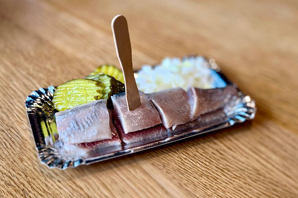 Amersfoort, The Netherlands. November 6th, 2025: Close-up of a traditional Dutch delicacy — raw herring served on a small tray with sliced pickles and chopped onions. This classic street food is a beloved part of Dutch culinary culture, often enjoyed fresh from the fish stall with a wooden pick.