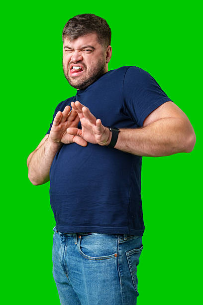 istock A man with a serious expression holds up both hands in a stopping gesture against a bright green background 2245276199