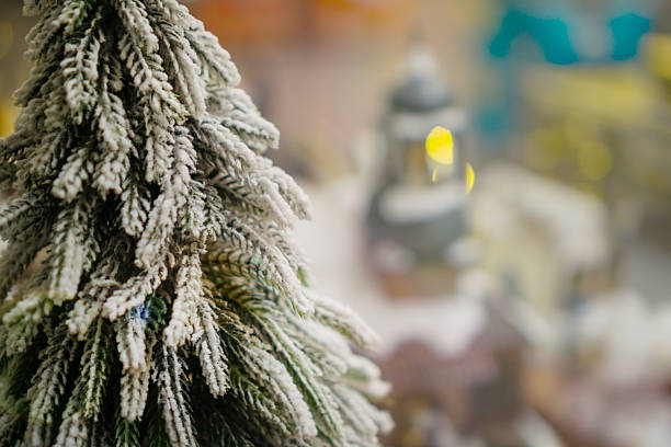 a snow covered miniature pine tree with bokeh lights and soft snowfall effect in a Christmas village concept of holiday advertising, winter celebration, festive greeting.