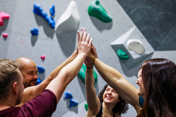 A diverse group celebrates a climbing session with high fives, showcasing teamwork, motivation, and camaraderie in an indoor bouldering gym setting.