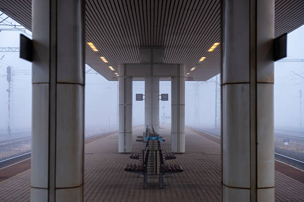 Budapest, Hungary - December 19, 2024: Empty railway platform stretches into dense fog, with benches lined under a roof and signals faintly visible in the distance.