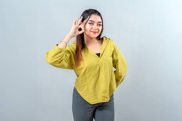 istock Confident young Asian woman smiling while making an OK hand gesture. Her bright expression and direct eye contact convey approval, assurance, and positivity for promotional use. 2245297845
