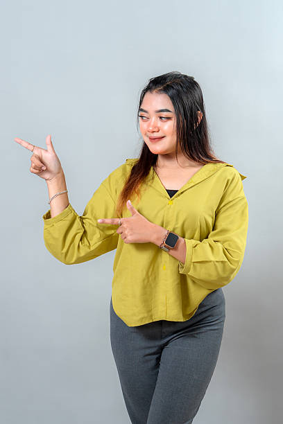 istock Smiling young woman pointing with both hands while looking confidently at the camera. Her cheerful expression and positive body language make her stand out. 2245297957