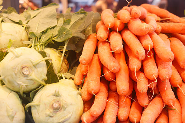A horizontal still life of a head of cauliflower, two whole carrots, and a vibrant vine of red cherry tomatoes, arranged on sunlit white linen. The soft natural light highlights the fresh textures and rich colors of these nutrient-packed vegetables. This scene celebrates seasonal produce and the principles of mindful eating, sustainable living, and home gardening. A quiet homage to the superfoods that support well-being and connect us to the rhythms of nature and the harvest.