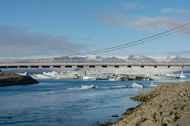 istock A bridge spans over glacier-filled waters, with snow-capped mountains afar. 2245300974