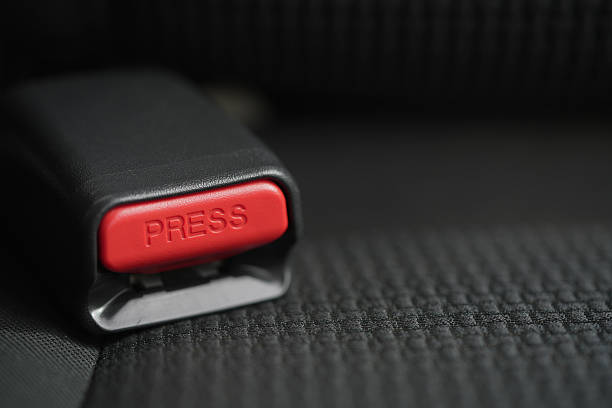 Macro shot of a car's seatbelt receptacle, highlighting the red release button. Emphasizes road safety on a dark background with copy space for text
