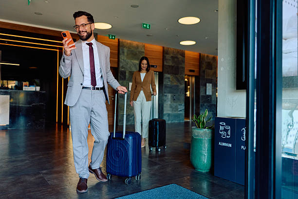 istock Businessman checking smartphone at hotel lobby with luggage 2245302592