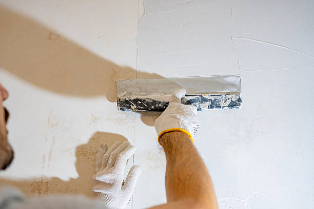 istock Over-the-shoulder view of a skilled worker's gloved hands applying and smoothing a layer of fresh plaster or joint compound onto an interior wall during renovation. 2245303669