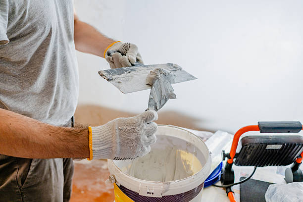 istock Close-up of a renovation worker's gloved hands preparing to plaster, loading a large smoothing trowel with joint compound from a smaller hand spatula over a material bucket 2245303674