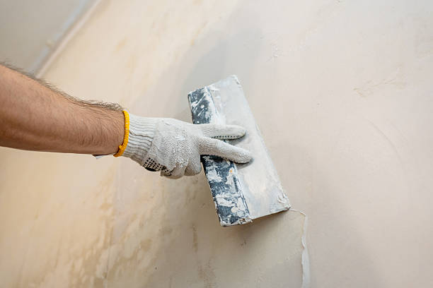 istock Surface preparation in progress: A worker carefully pushes and spreads fresh spackle or plaster across an interior wall for optimal smoothness before painting 2245303682