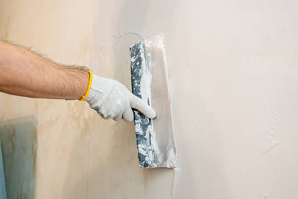 istock Surface preparation in progress: A worker carefully pushes and spreads fresh spackle or plaster across an interior wall for optimal smoothness before painting 2245303691