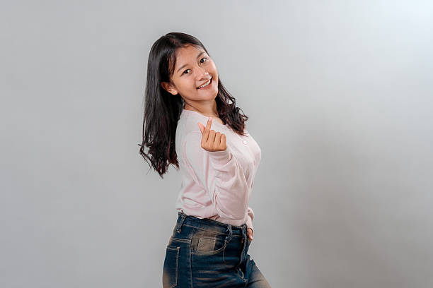 istock Cheerful young Asian woman smiling brightly while making a finger heart gesture with a playful expression, showing positivity and friendliness in a neutral studio background. 2245304340